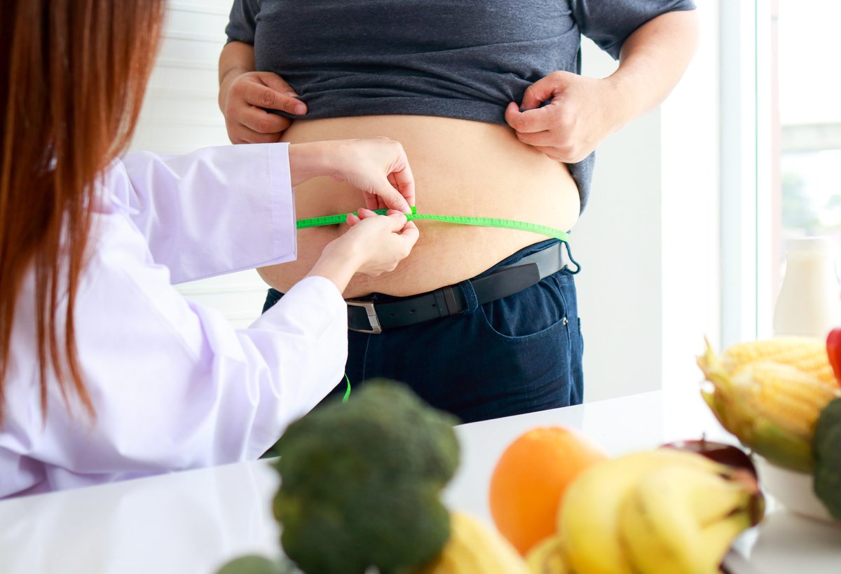 Profissional de saúde medindo a circunferência abdominal de um paciente com fita métrica, ao lado de frutas, no tratamento da obesidade